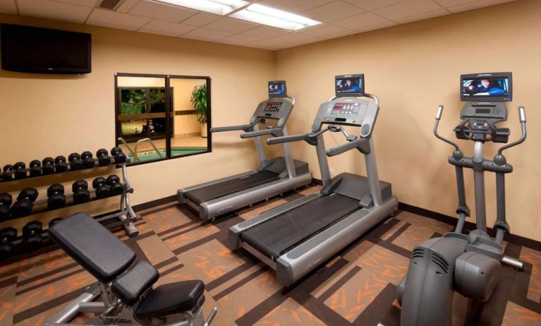 Sonesta Select Miami Lakes’ fitness center is equipped with various exercise machines, free weights, and a wall-mounted TV.