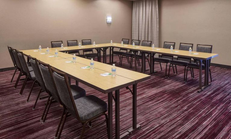 Hotel meeting room with tables arranged in a U-shape and seating for over a dozen attendees.