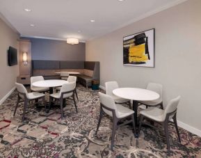 Lobby lounge in Sonesta ES Suites Atlanta Alpharetta North Point Mall with small tables and both art and a large TV on the wall.