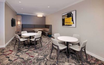 Lobby lounge in Sonesta ES Suites Atlanta Alpharetta North Point Mall with small tables and both art and a large TV on the wall.
