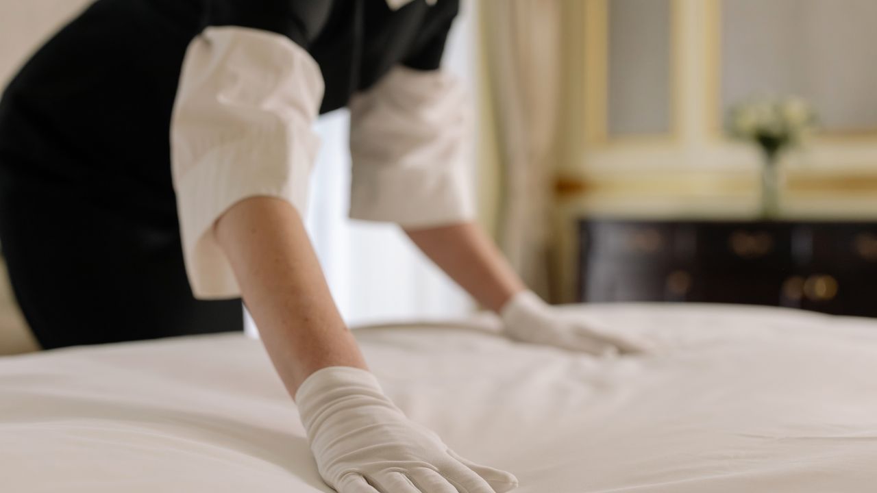 how to check for bed bugs in a hotel room: housekeeper wearing gloves and changing hotel bed sheets