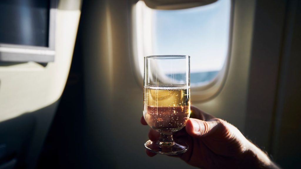 can you drink your own liquor on an airplane: hand hold a sparkling wine with an airplane window as background
