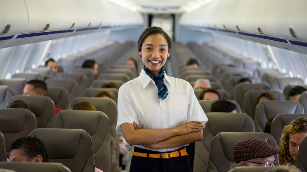 flight attendant explains faa rules: flight attendant stands in aisle with arms crossed