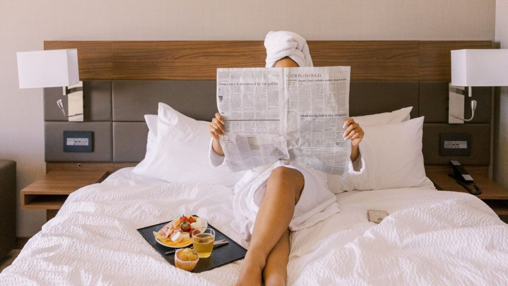 why do hotels use white bed linens: lady reading a newspaper and having breakfast in bed