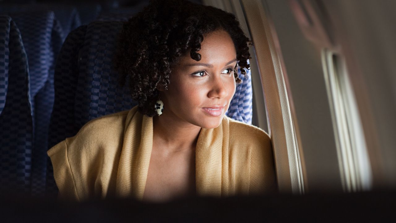foods you should avoid before and during your flight: lady with curly hair gazing out of the airplane window