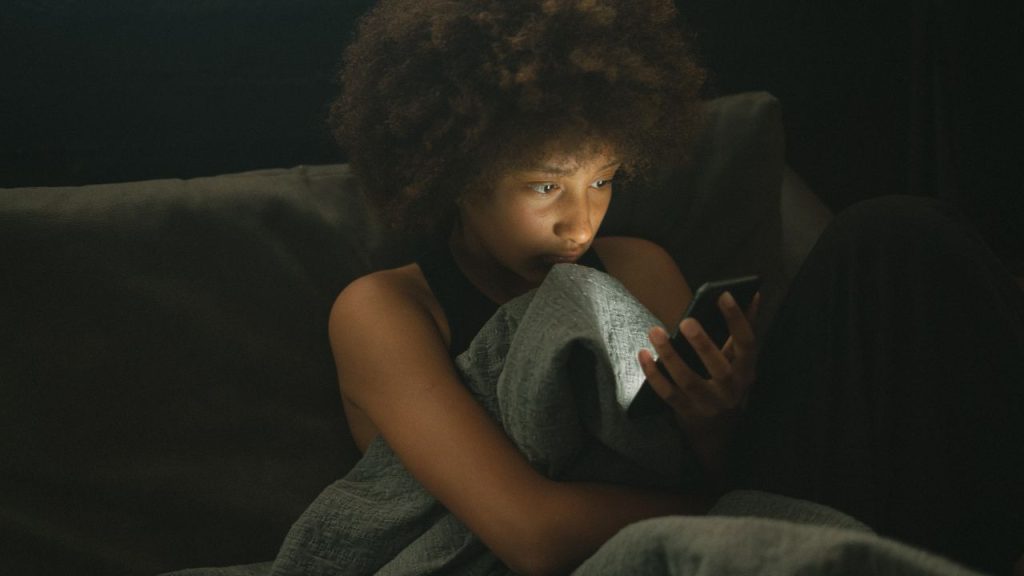 technology causes sleeplessness: lady sitting up in bed scrolling on her cell phone