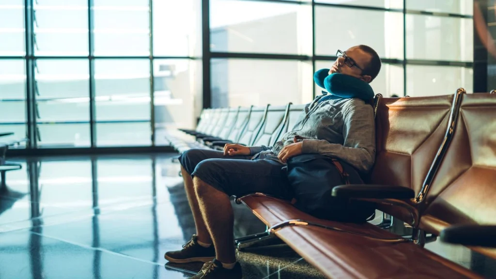 young man sleeping in airport upright while awaiting his flight.