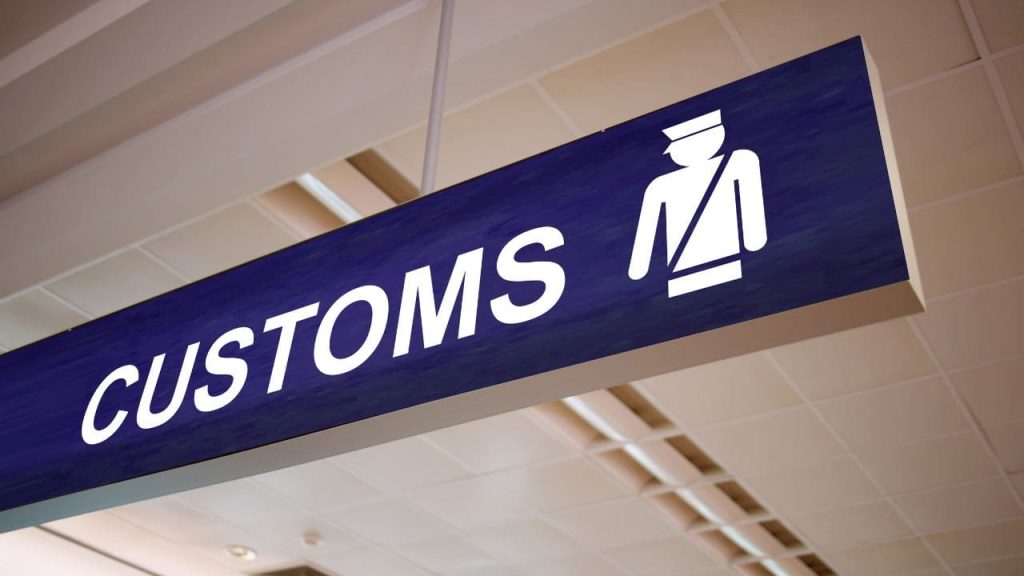 Overhead customs sign indicating border control checkpoint at airport terminal.