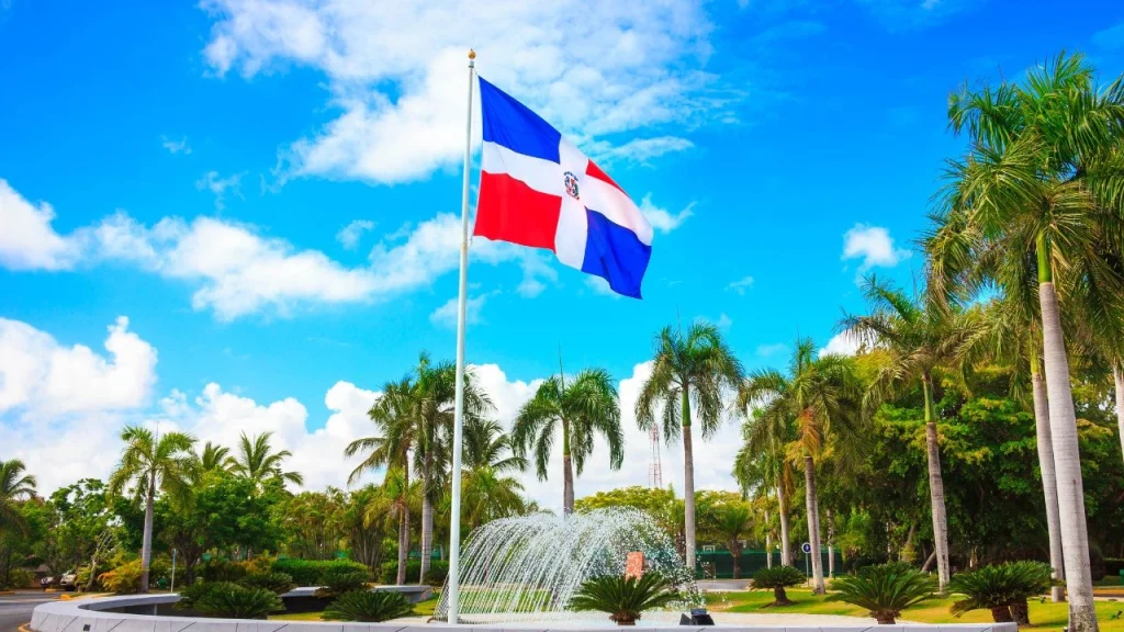 dominican republic flag flying with a water feature and palm trees in the background