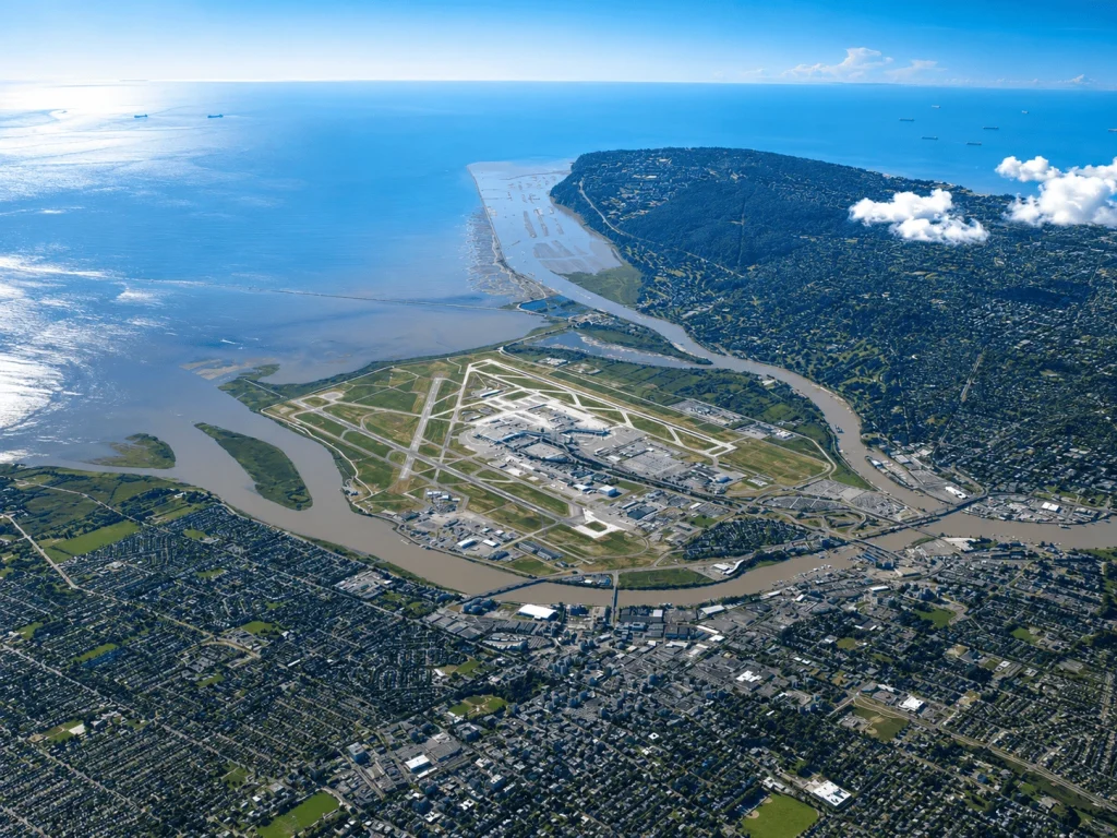 Aerial view of Vancouver International Airport (YVR) on Sea Island, showing the terminal, runways, Fraser River, and surrounding Vancouver-area neighborhoods.