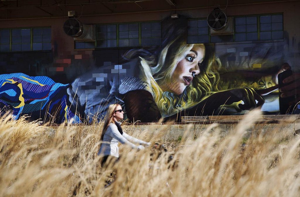 A bicyclist passes a mural of a woman touching her phone along the BeltLine in Atlanta.