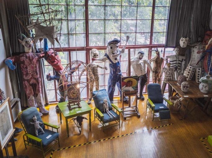 A variety of multi colored life size puppets lean against a floor to ceiling glass window grid.