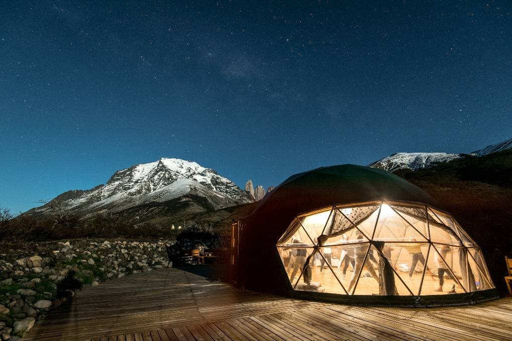 People doing yoga in lit up interior dome at night in mountains.