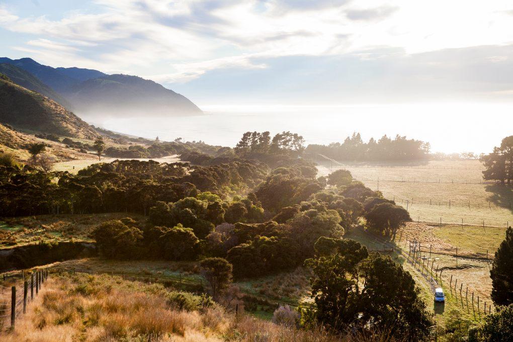 Sun shining down on pasture, water and mountains.