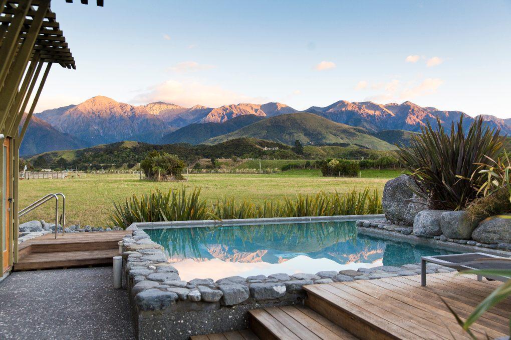 Jacuzzi overlooking calm green pasture and mountain backdrop.