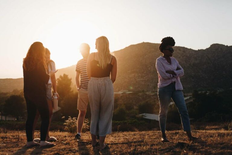 Group of young people standing and chatting outside in mountainous desert with sun shining. 