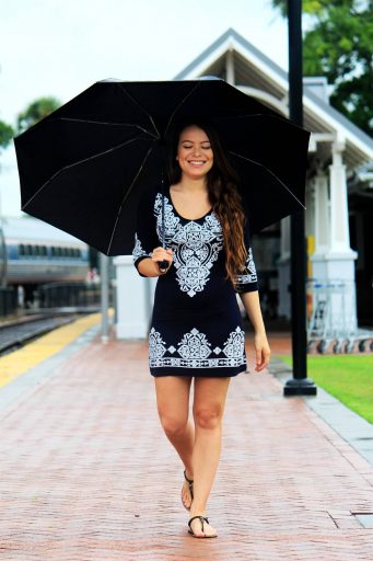 Woman in dress walking with umbrella on gray day.