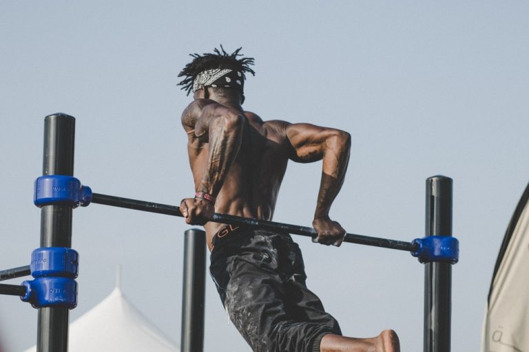 Ripped man hoists his body up on outdoor gym bars with muscles rippling.