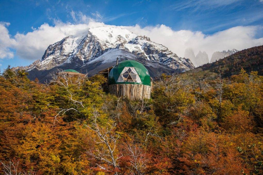 Green dome rises above trees with mountain backdrop.