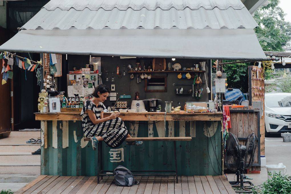 Woman sits and reads at kitchen and bar area of The Yard Hostel in Bangkok, Thailand