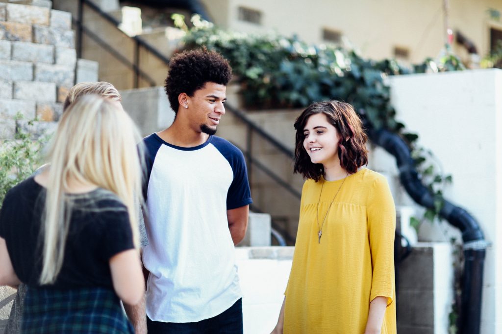 One man and two women stand in circle and have conversation outside. 