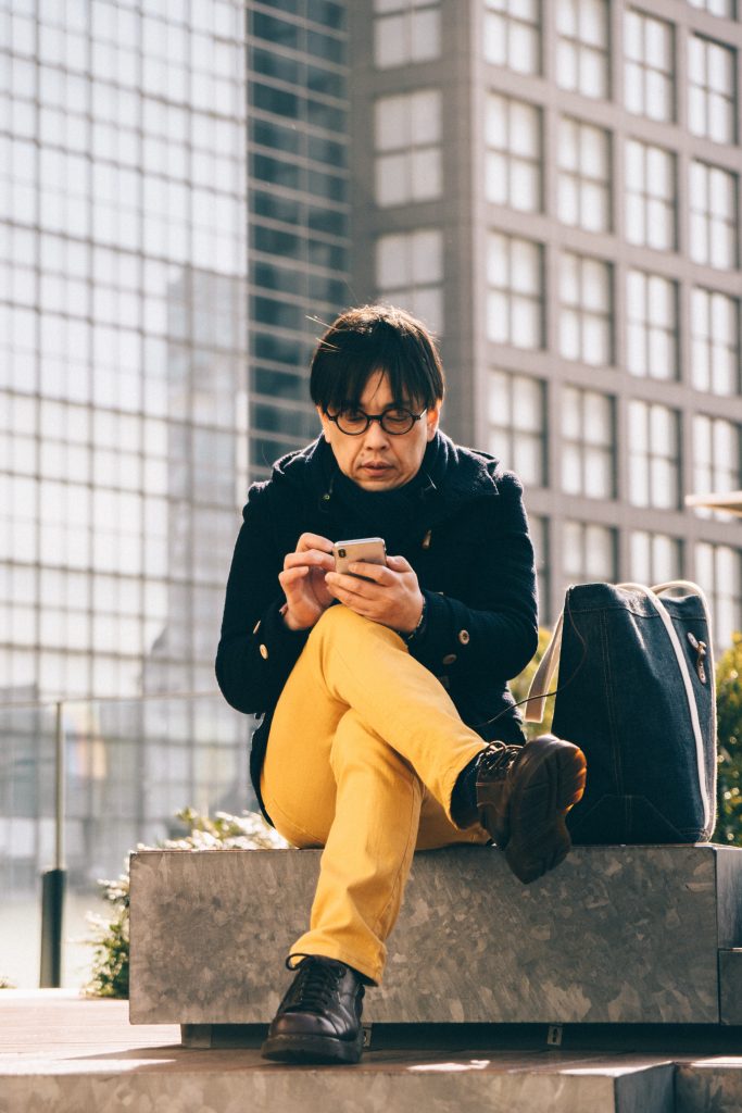 Middle-aged man with glasses sitting down in yellow pants using smartphone.