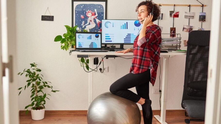 ergonomic tips for remote workers: lady standing at her home office desk using a yoga ball for stability while talking on the phone
