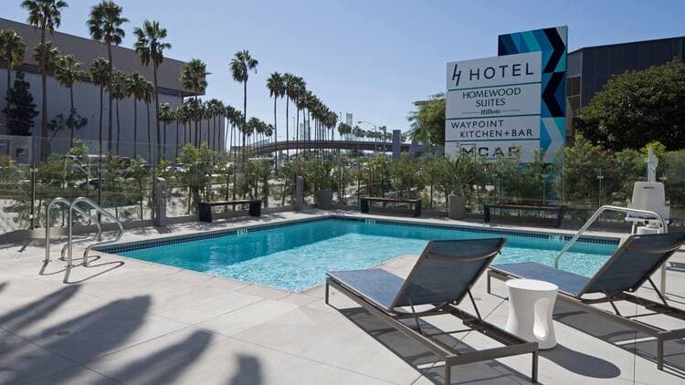 Lounge pool chair overlooking pool and clear blue skies with palm trees.