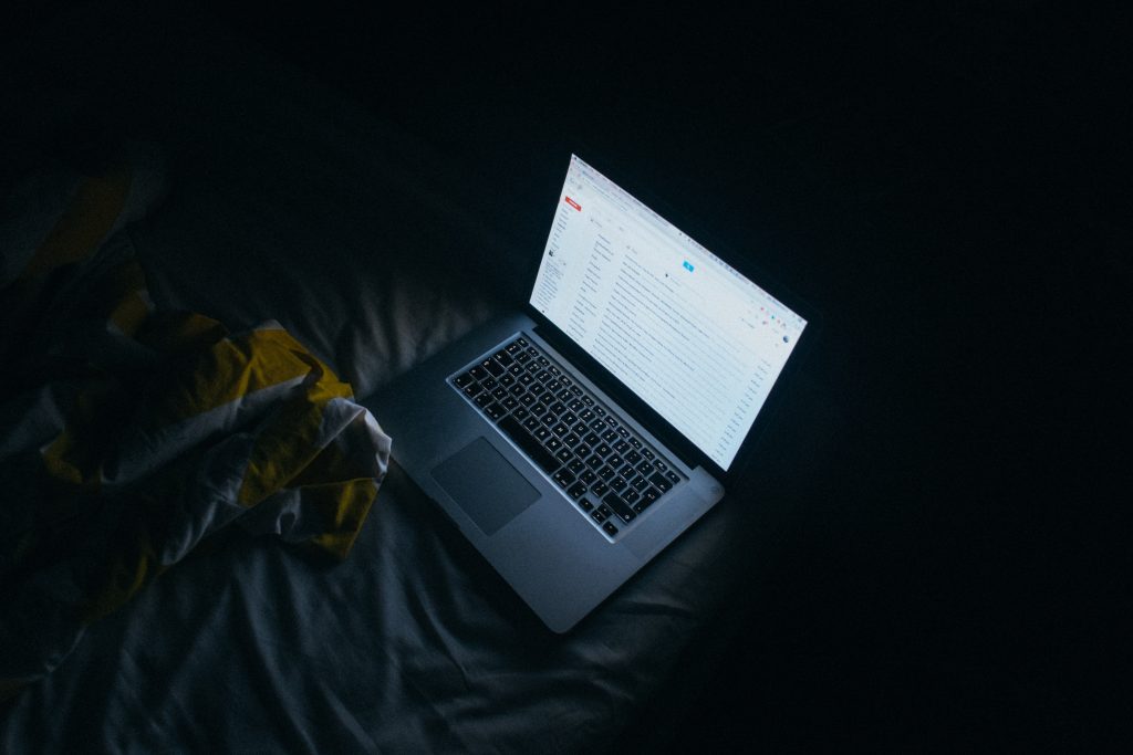 Laptop on bed at night showing emitting a blue screen and showing an email inbox.