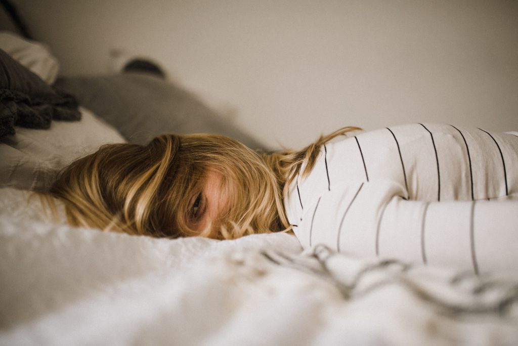 Woman laying face down on bed with eyes wide open.
