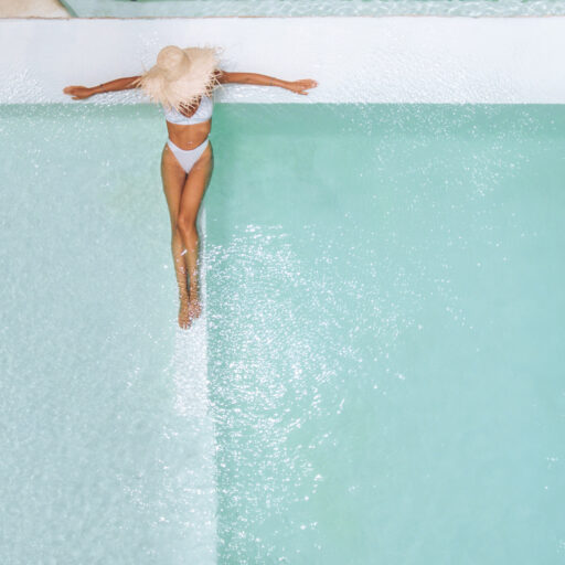 Woman in straw hat relaxing in clear water of pool on hot summer day.