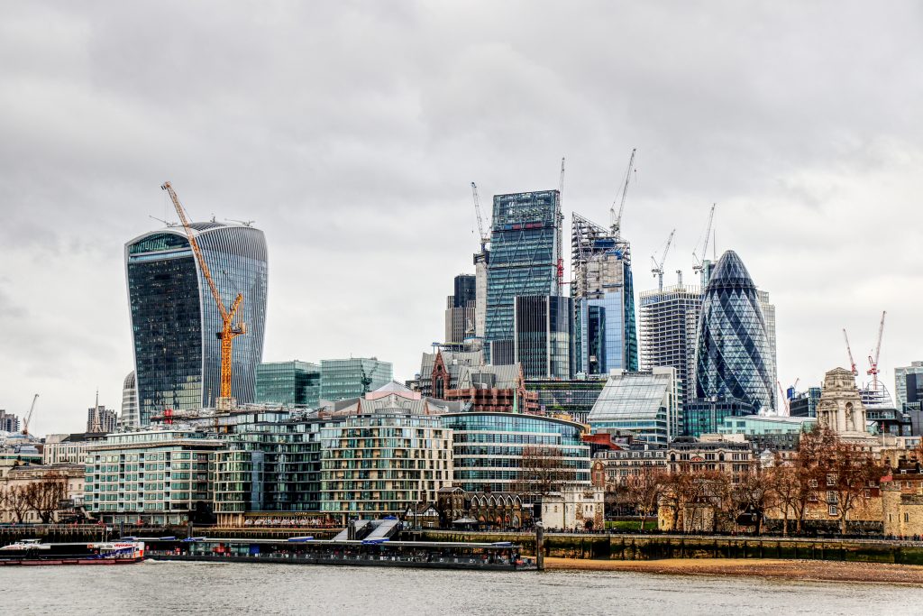 A backdrop from the Thames River of London's modern architecture juxtaposed by smaller, historical buildings.