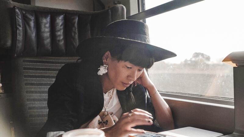 Woman looks at phone while sitting in train car, window to her left.