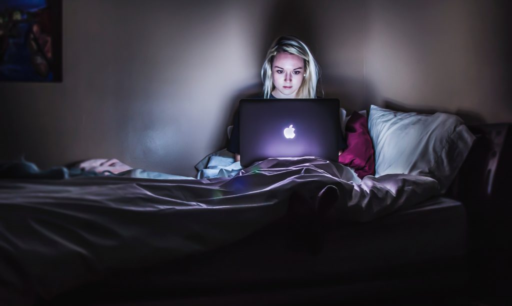 Lady working on her MacBook Pro in bed at night, the laptop glow filling the room. 