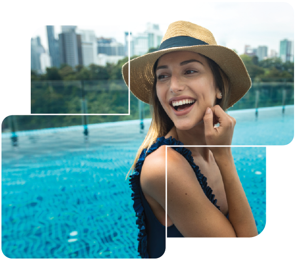 Woman in a straw hat smiling by an outdoor pool with a city skyline in the background